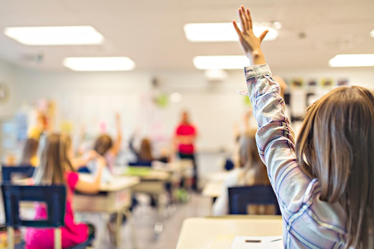 A student in the back of an elementary school classroom raises her hand.