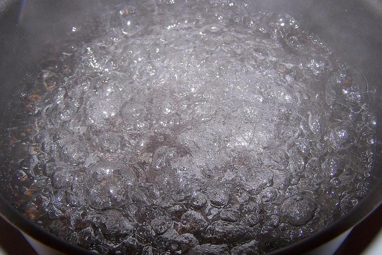 Water boils on a stove. Municipalities can issue boil water notices when water pressure drops, pipes break or germs increase in drinking water.