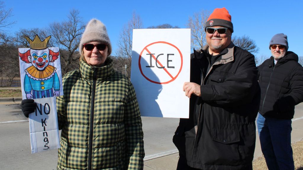 Woman holds "No Kings" sign next to two men holding signs against ICE