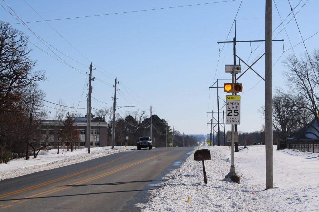 cars drive past school zone sign in snow