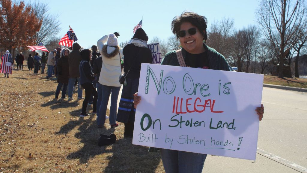 Woman holding sign saying "no one is illegal on stolen land" at protest