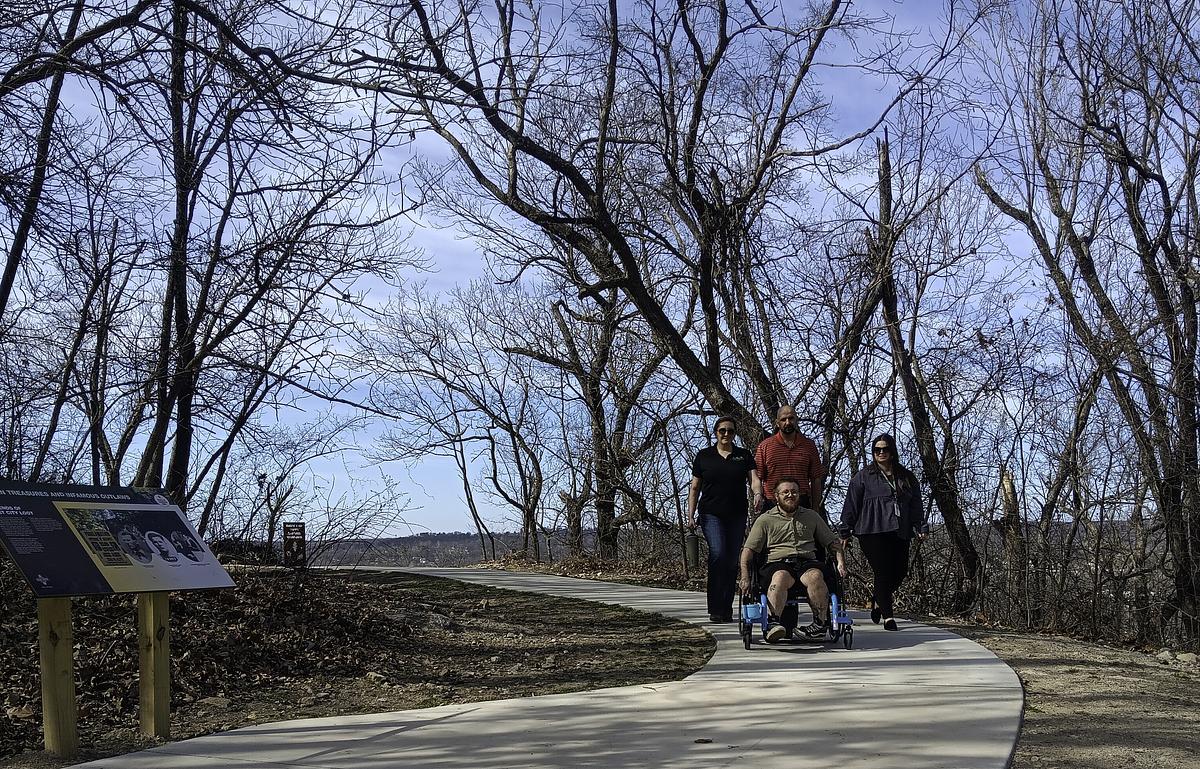 Finnigan Bark (front), Laurie Biby of the Tulsa Urban Wilderness Coalition, Tulsa County Parks Director Matt Hancock and Tulsa County Parks Communications Manager Karsten Villanueva walk down Chandler Park's newly completed wheelchair accessible trail.