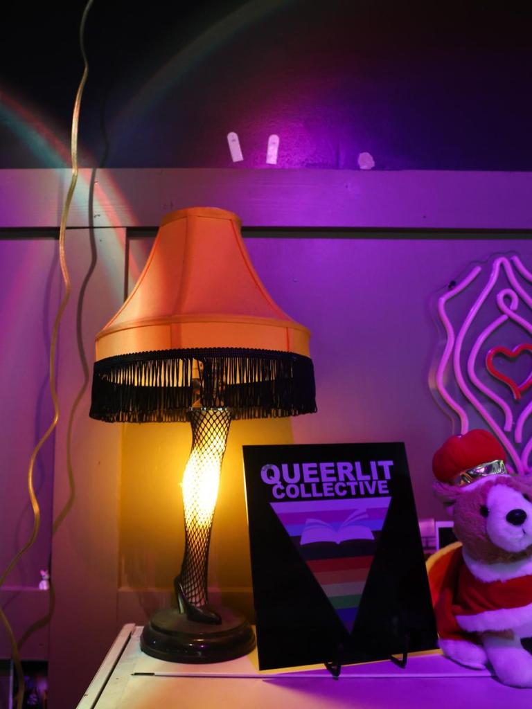 Signage for Queer Lit Collective beside a leg lamp on a book shelf in YBR Pub.