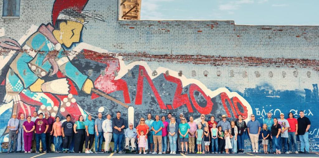 Employees of Osage Nation's language department and others gather in front of a new mural in Pawhuska that incorporates Osage language.