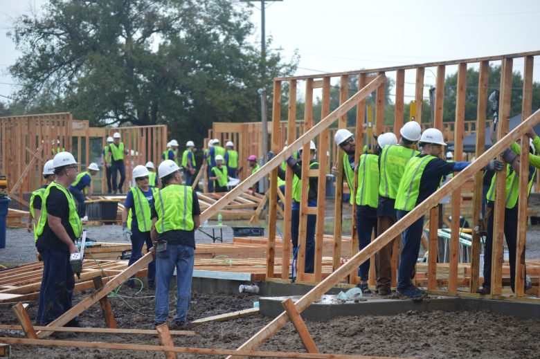 People in green vests put up wooden walls for a home